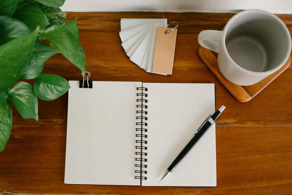 From above empty notebook with pen and tags placed near potted plant and empty mug on office table