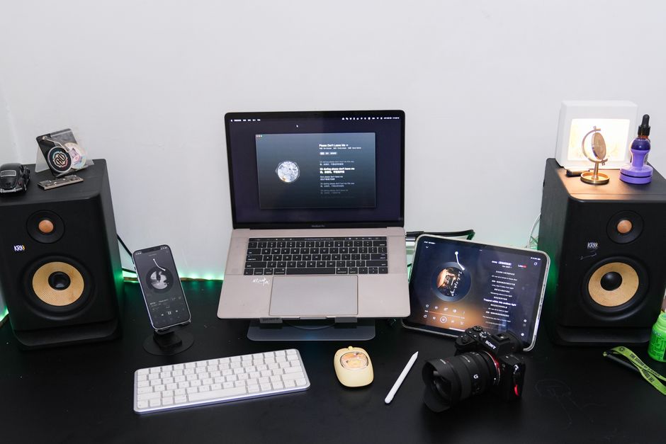 A modern home studio desk setup featuring a laptop, speakers, tablet, smartphone, and camera equipment for creative workspaces.